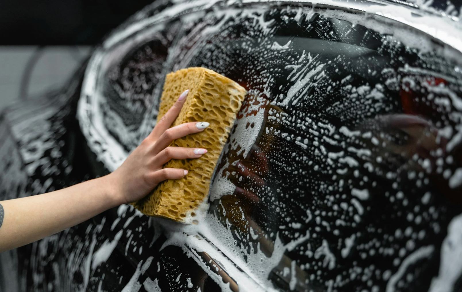 close-up of a hand cleaning a car with a sponge 
