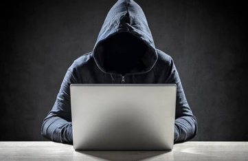 hooded stranger behind a laptop for Scams to Be Aware of When Selling a Car.
